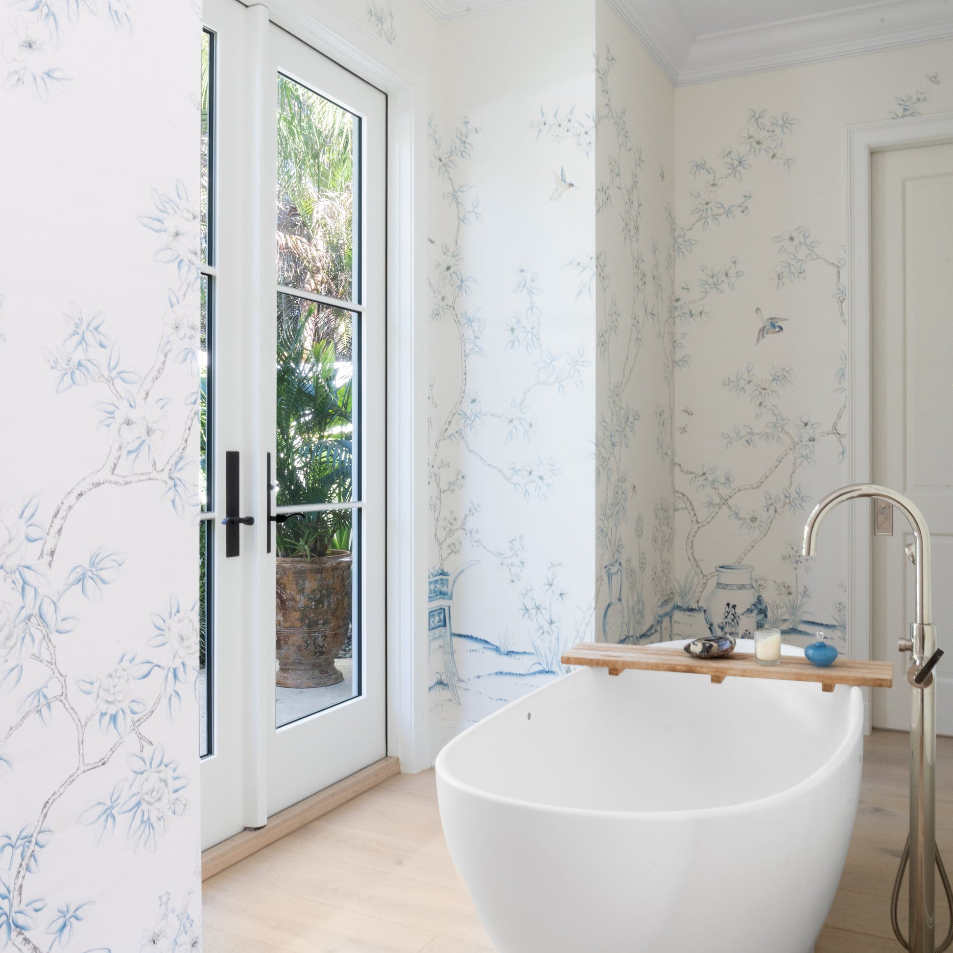 Modern bathroom with freestanding bathtub, mural wallpaper, and glass door.