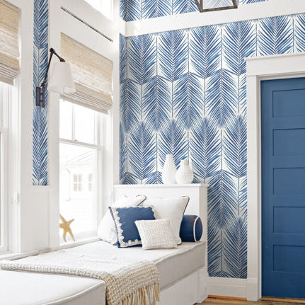 Room interior with blue and white patterned wallpaper, a window seat with pillows, and a blue door.