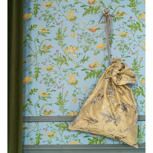 Gold fabric bag with floral patterns on a blue floral wallpaper background
