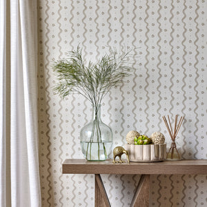 Decorative table with a vase, bowl of fruit, and diffuser against a patterned wallpaper.
