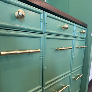 A mint green cabinet with a bamboo-style drawer front design, featuring brass-toned round knobs and bar handles, shown in a close-up interior shot.