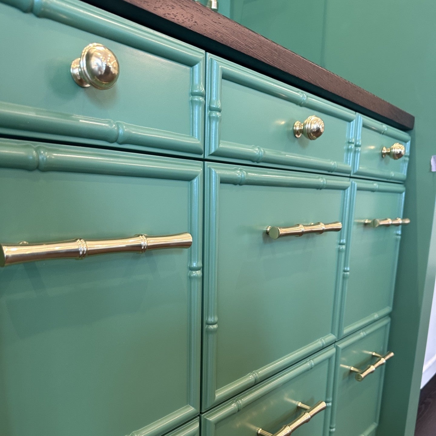 A mint green cabinet with a bamboo-style drawer front design, featuring brass-toned round knobs and bar handles, shown in a close-up interior shot.