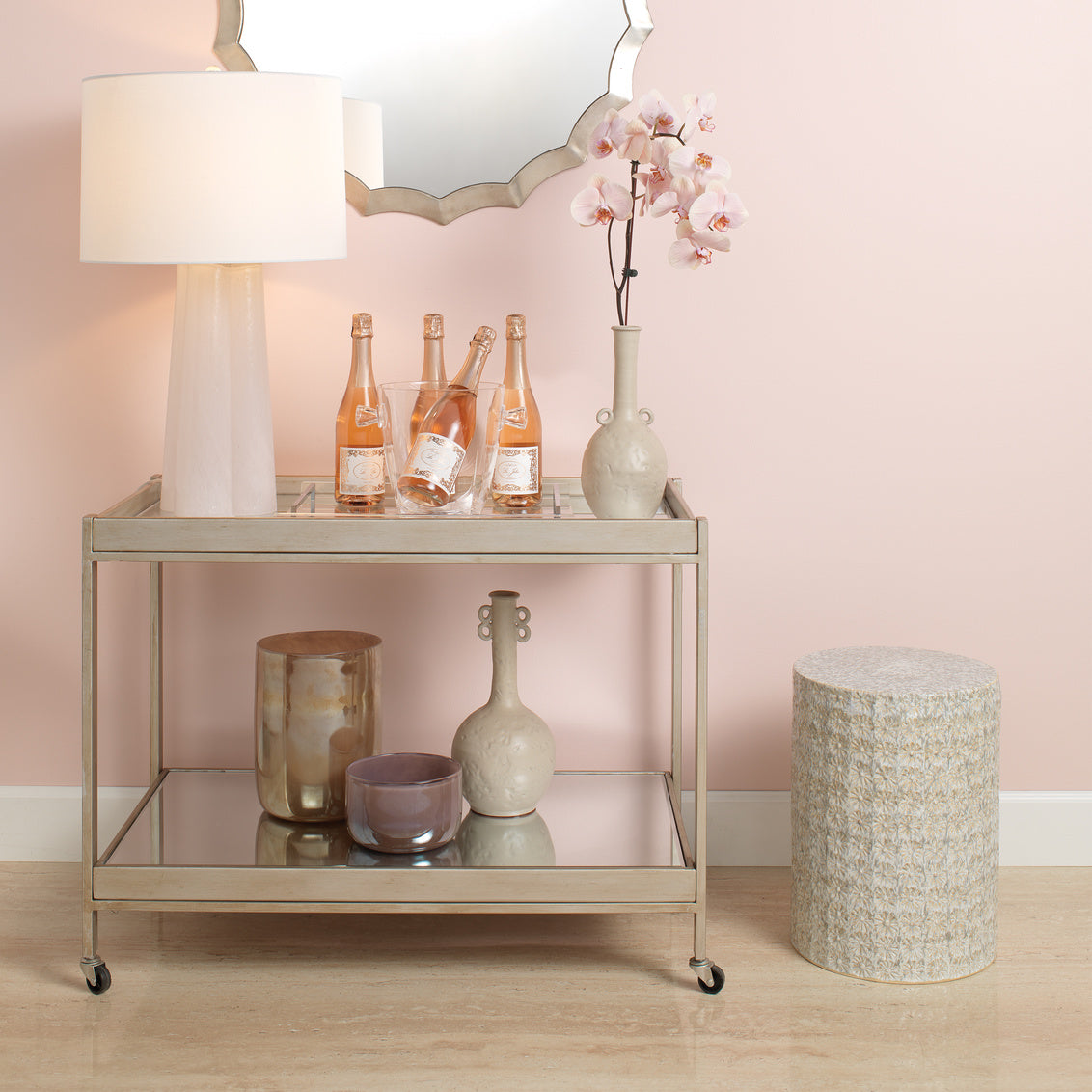Decorative cart with bottles, vases, and a lamp against a pink wall.