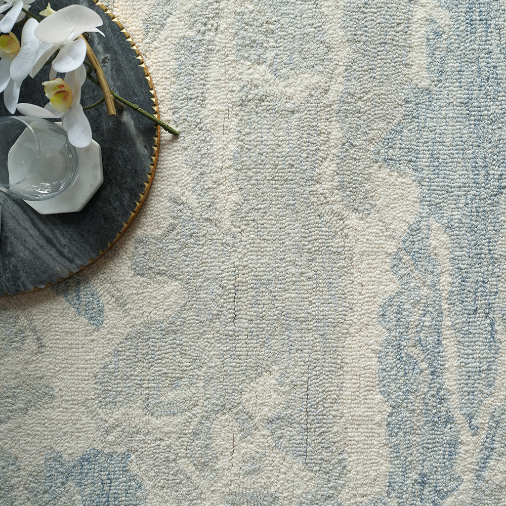 Textured blue and beige rug with a decorative plate and flowers on a light background
