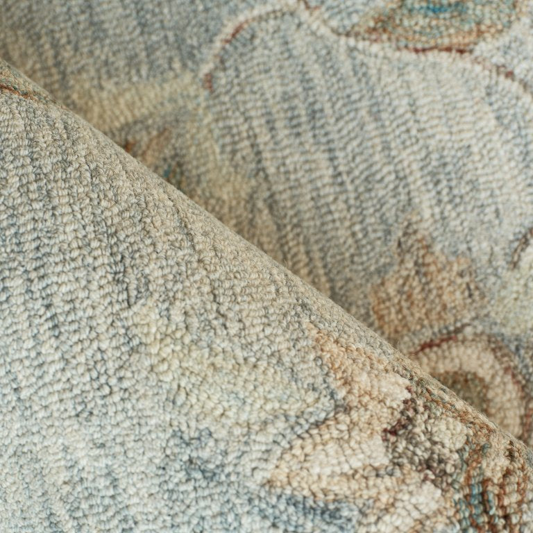 A close-up of a textured area rug with a vintage floral pattern in muted tones of beige, gray, and light blue.