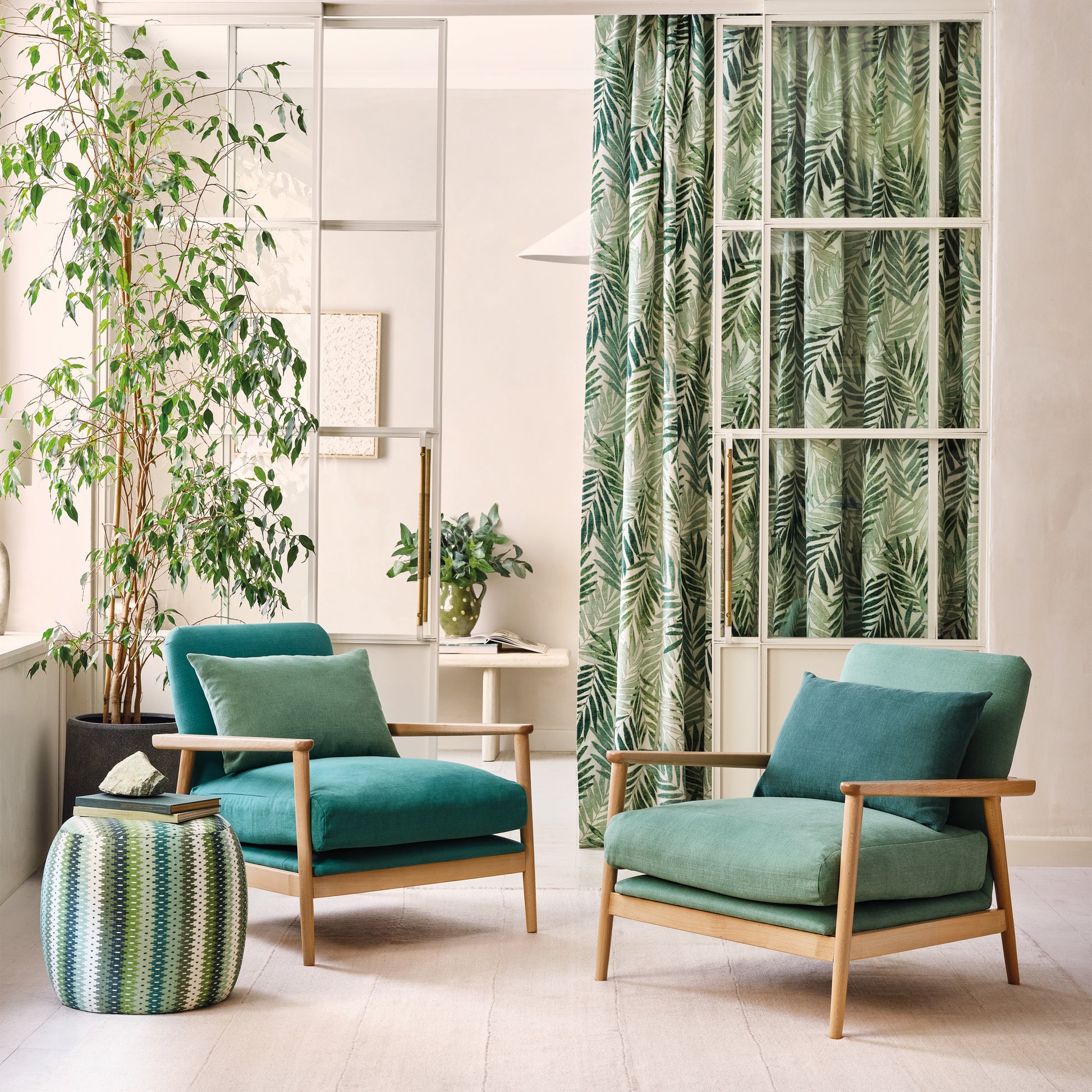 Modern living room with teal armchairs, ottoman, and decorative plants.