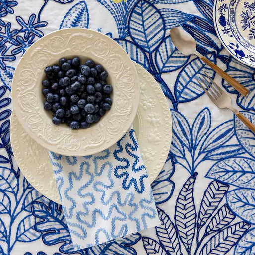 Table setting with blueberries on a decorative plate over a blue and white patterned fabric.