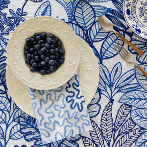 Table setting with blueberries on a decorative plate over a blue and white patterned fabric.