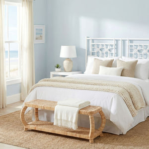 Bedroom with a bed, rattan bench, and lamp in a bright room.