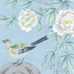 A traditional-style botanical illustration featuring pale blue-green leaves, large white and blush flowers, and a small bird perched on a tree stump against a soft light blue background.