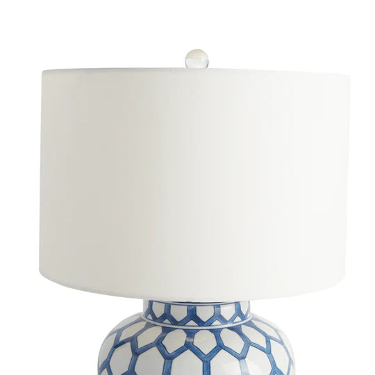 Table lamp with white shade and blue geometric patterned base on a white background
