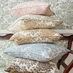 Stack of patterned pillows on a chair with a floral wallpaper background
