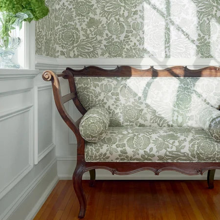 Decorative sofa with floral patterned cushions against a matching wall in a room with wooden flooring.