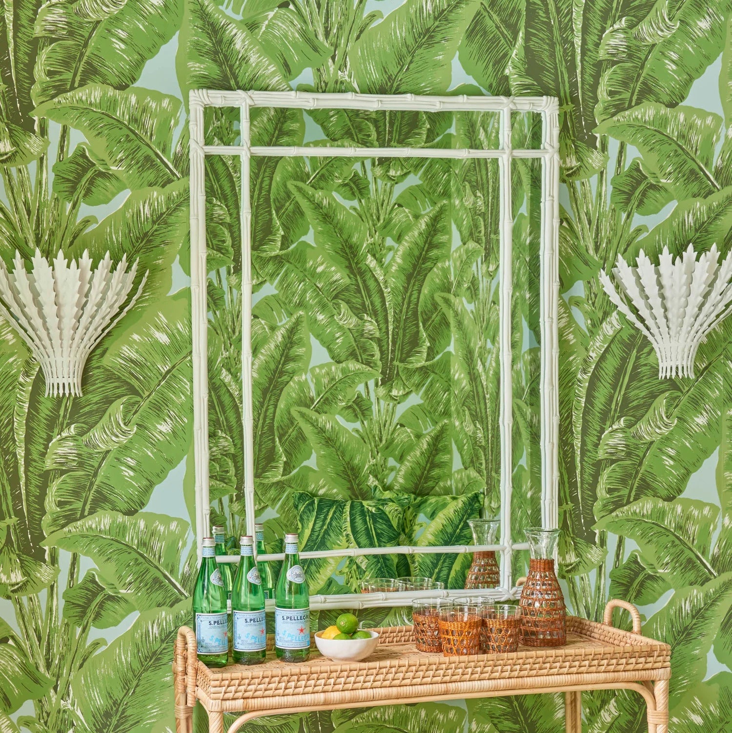 Installation of Banana Palm Leaves wallpaper in green and aqua behind a bar cart flanked by white sconces