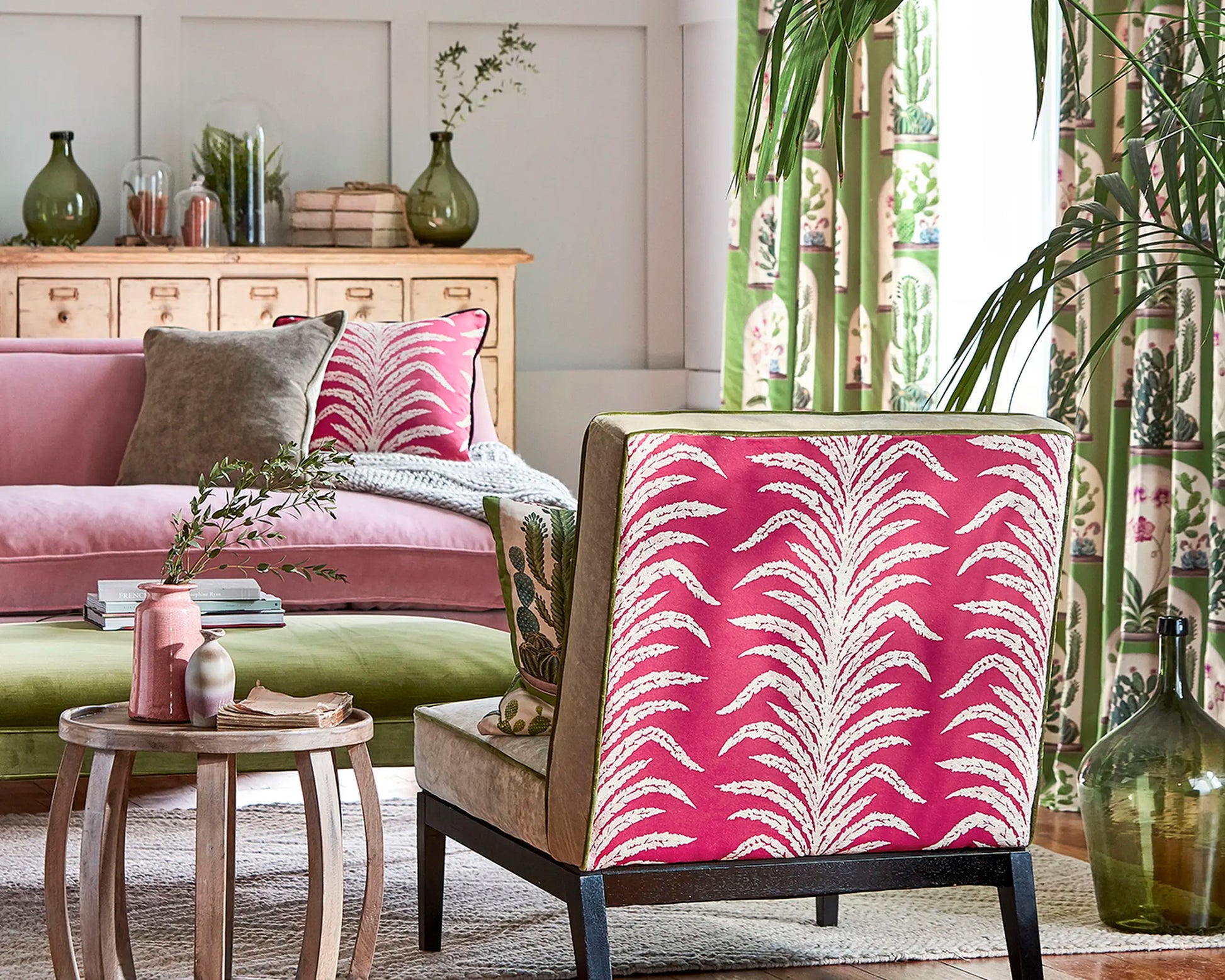 Living room with pink patterned chair and sofa, decorative pillows, and a small table.