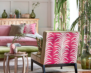 Living room with pink patterned chair and sofa, decorative pillows, and a small table.