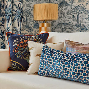 Decorative pillows on a sofa with a patterned lamp and wallpaper in the background