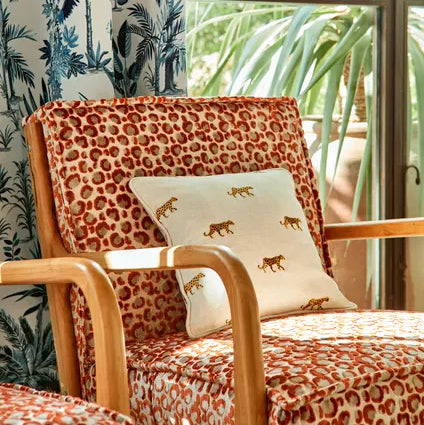 Chair with leopard print fabric and a decorative pillow in a room with a window showing greenery.