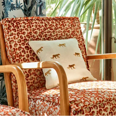 Chair with leopard print fabric and a decorative pillow in a room with a window showing greenery.