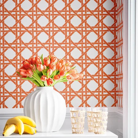 White table with a pumpkin, flowers, and bananas against a patterned orange and white wallpaper wall.