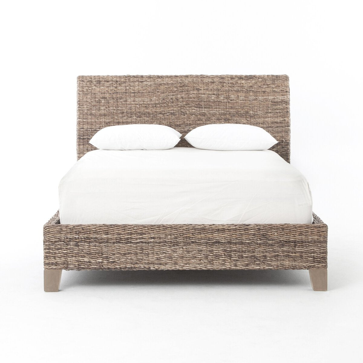 A woven seagrass bed shown with white bedding