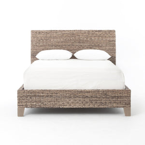 A woven seagrass bed shown with white bedding