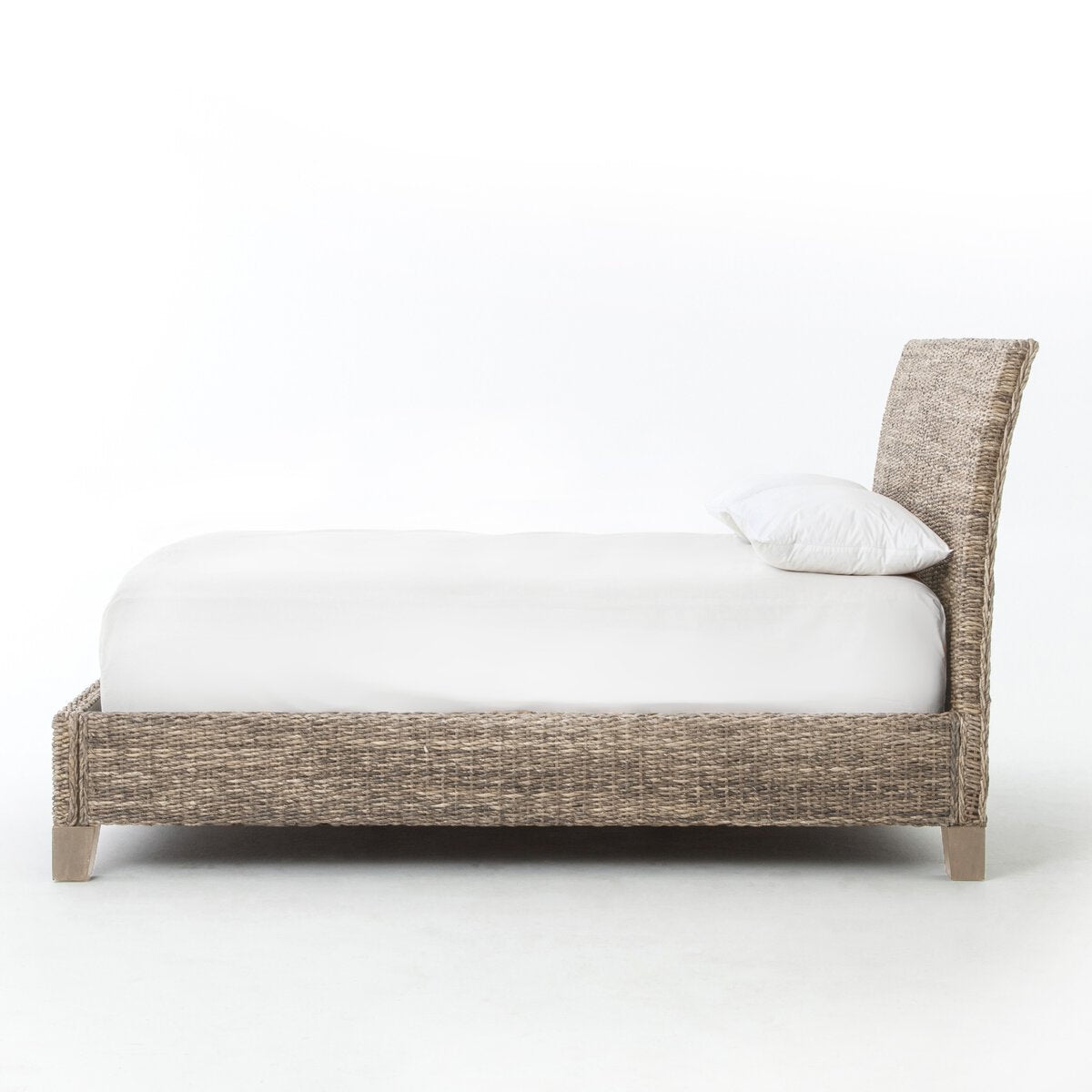 A woven seagrass bed shown from the side with white bedding