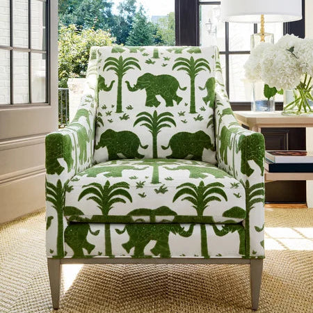 Chair with green elephant pattern in a room with large windows and a lamp.