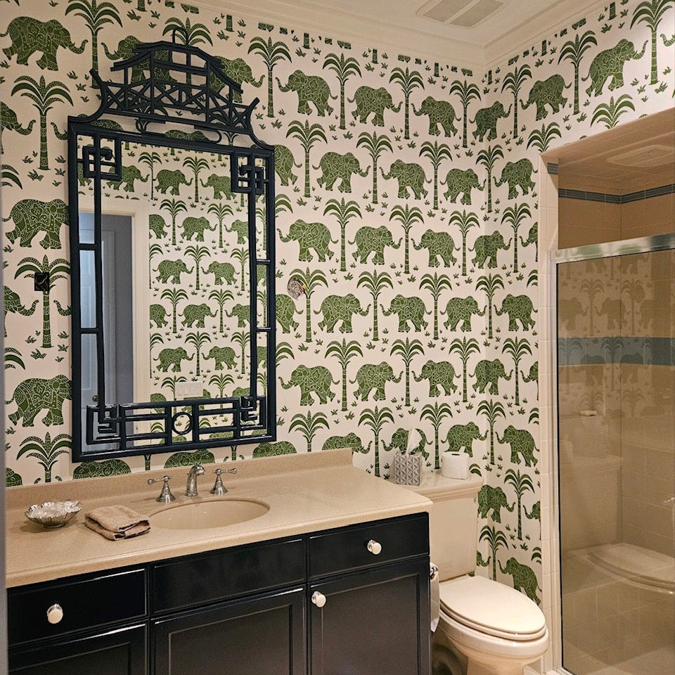 Bathroom with green elephant and palm tree patterned wallpaper, black vanity, and beige countertop.