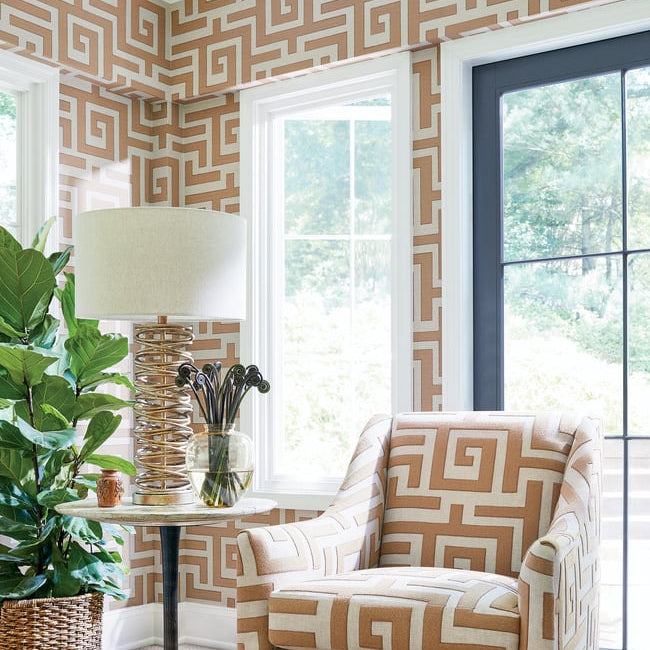 Living room with a patterned armchair, table, and lamp against a geometric wallpaper.