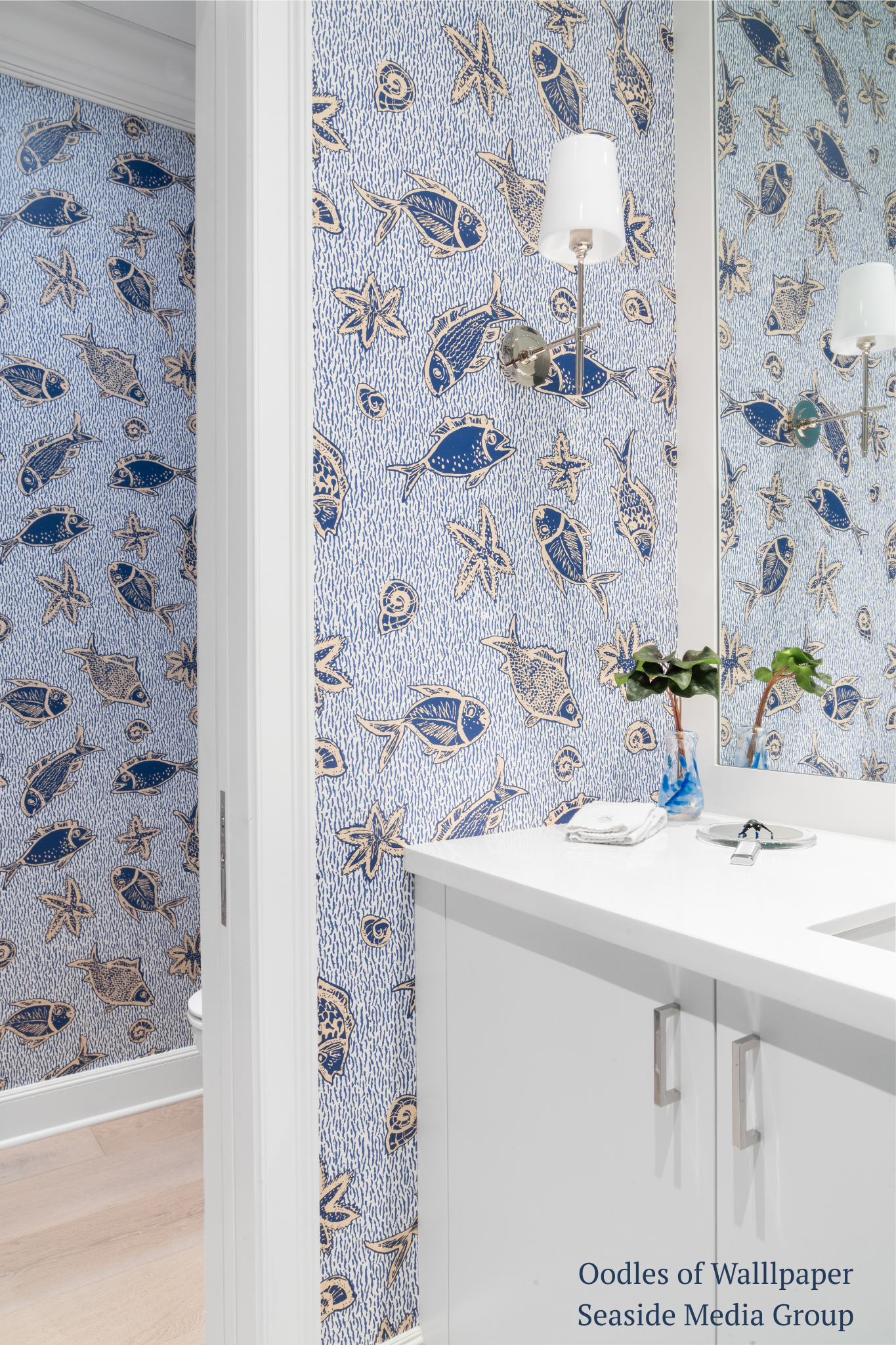 Bathroom with blue fish and sea-themed wallpaper, white cabinets, and a sink.