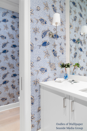 Bathroom with blue fish and sea-themed wallpaper, white cabinets, and a sink.