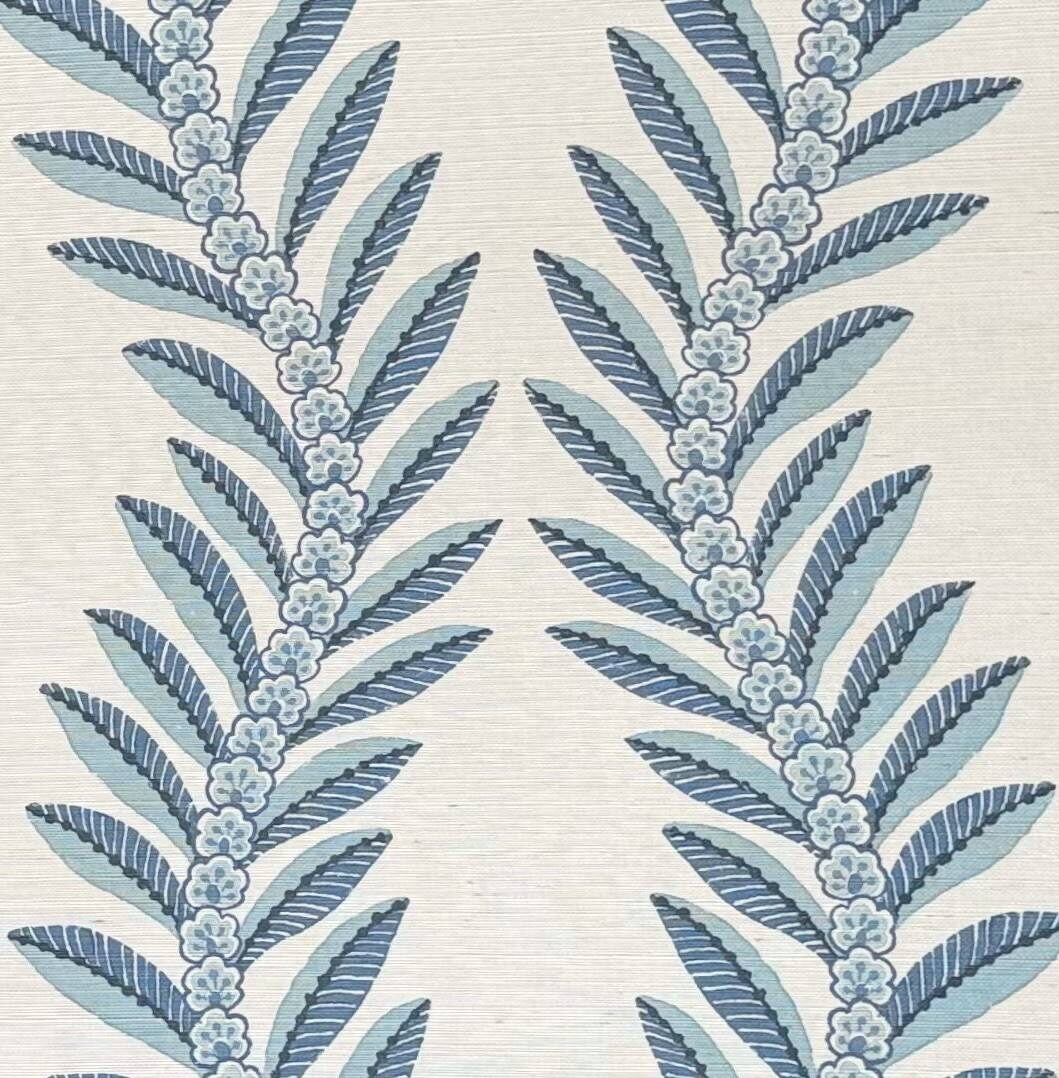 A close-up of a textile or wallpaper pattern featuring vertical botanical motifs with elongated leaves and small floral clusters in muted blue and pale blue on a warm off-white background.