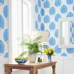 Room interior with wooden table, plants, and blue leaf-patterned wallpaper.