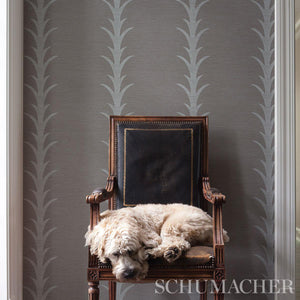 A section of grey wallpaper with a stylized stripe pattern based on a classic acanthus motif installed behind a chair 