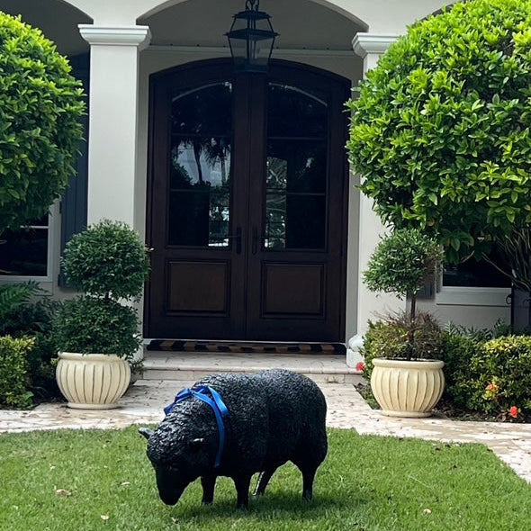 Black sheep sculpture grazing on a green lawn in front of a house with a dark wooden door.