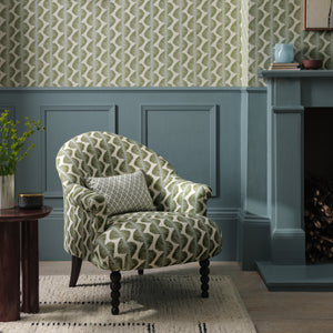 Patterned armchair in a room with green and white wallpaper, a fireplace, and a small table.