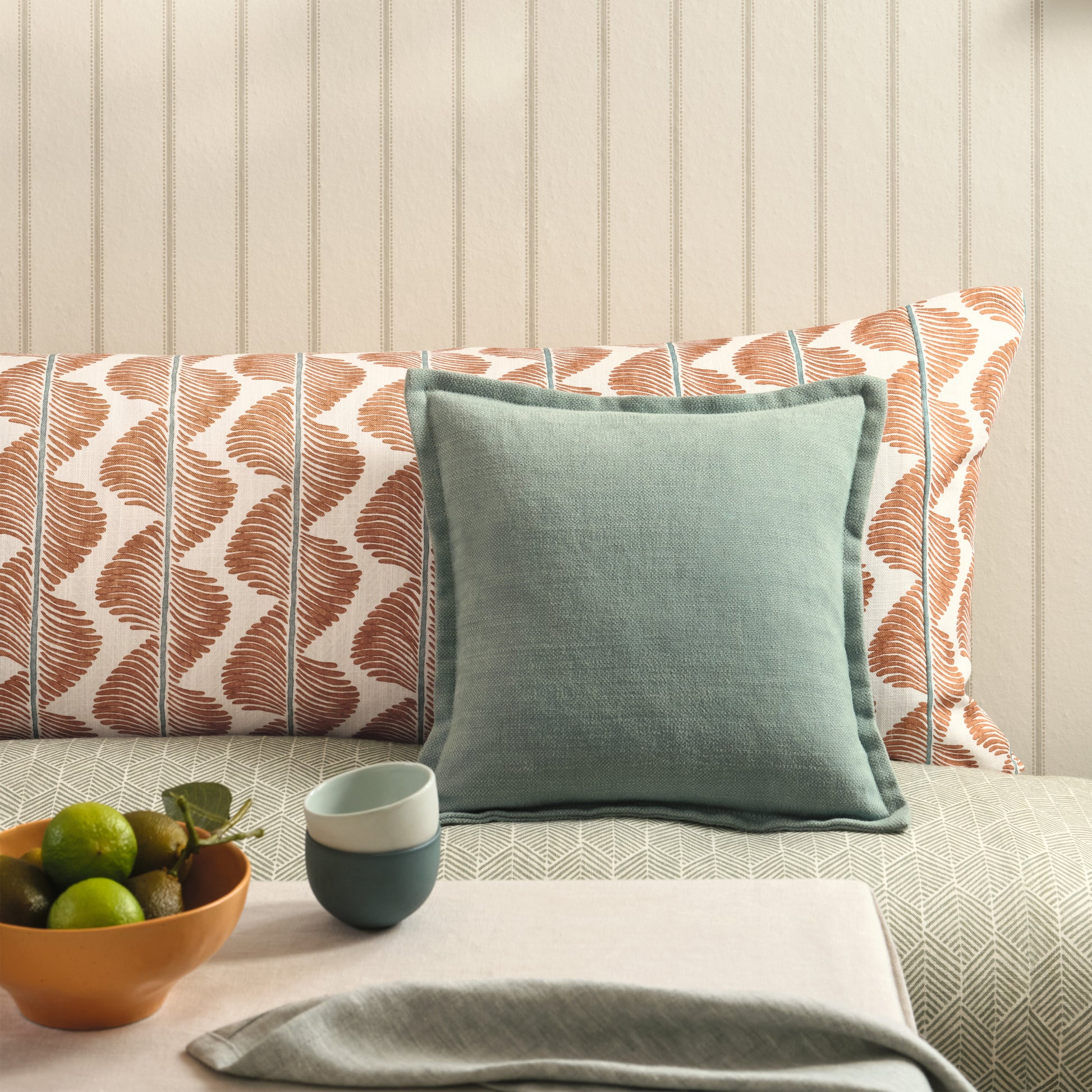 Decorative pillow on a sofa with a bowl of fruit and cups on a table in the foreground.