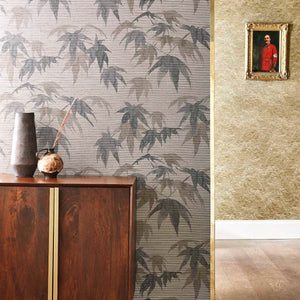 A wallpaper with a pattern of acer leaves in shades of gray and green installed on an accent wall with a chest in front 