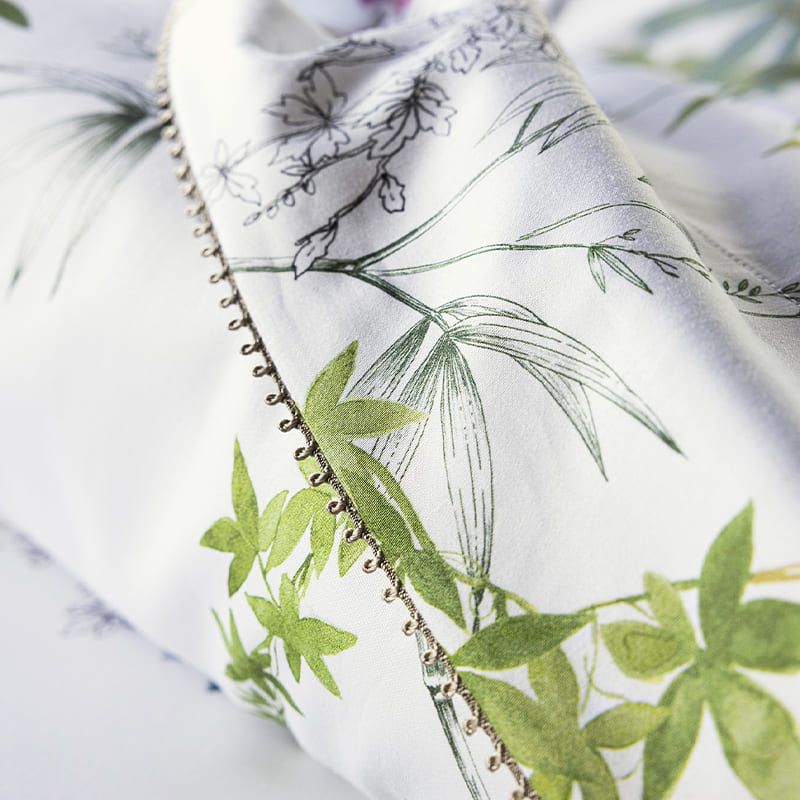 Close-up of bedding with green leaf pattern and metallic trim on a white background