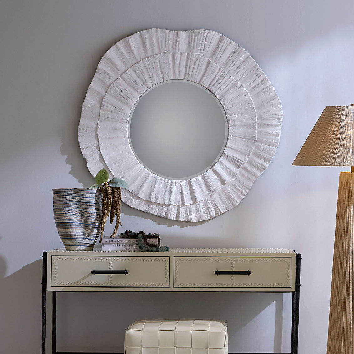 Decorative round mirror on a wall above a console table with a lamp and plant.
