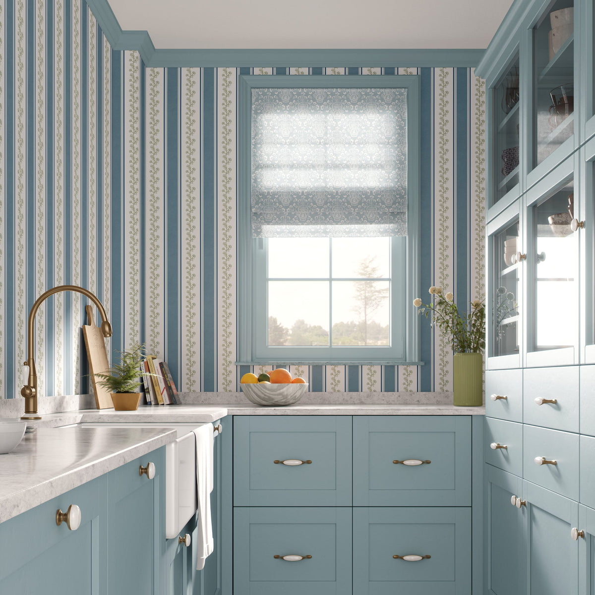 A beautifully styled kitchen featuring light blue cabinets, blue and white patterned wallpaper, a white marble countertop, a gold faucet, and a window with a sheer blue-gray roller shade.