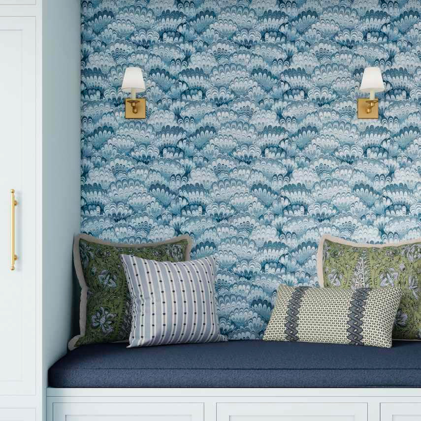 Nook with blue cushioned bench against a patterned wall, featuring decorative pillows.